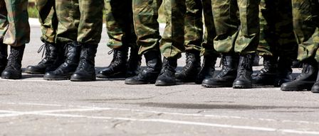 Eine Reihe von Soldaten in Tarnuniformen steht in Formation, ihre schwarzen Stiefel poliert. Die Umgebung scheint eine Parade oder eine formelle Veranstaltung zu sein.