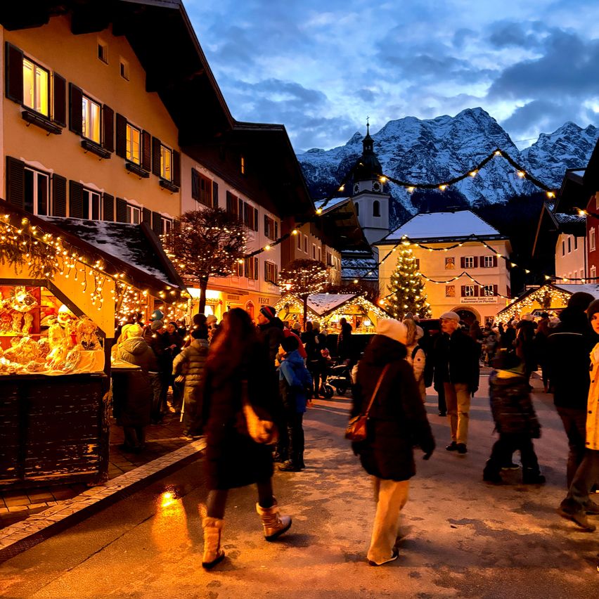 Ein Abend in einem europäischen Dorf. Es ist Winter, mit Schnee und Bergen im Hintergrund. Die Leute gehen durch die Stadt und besuchen Weihnachtsstände.