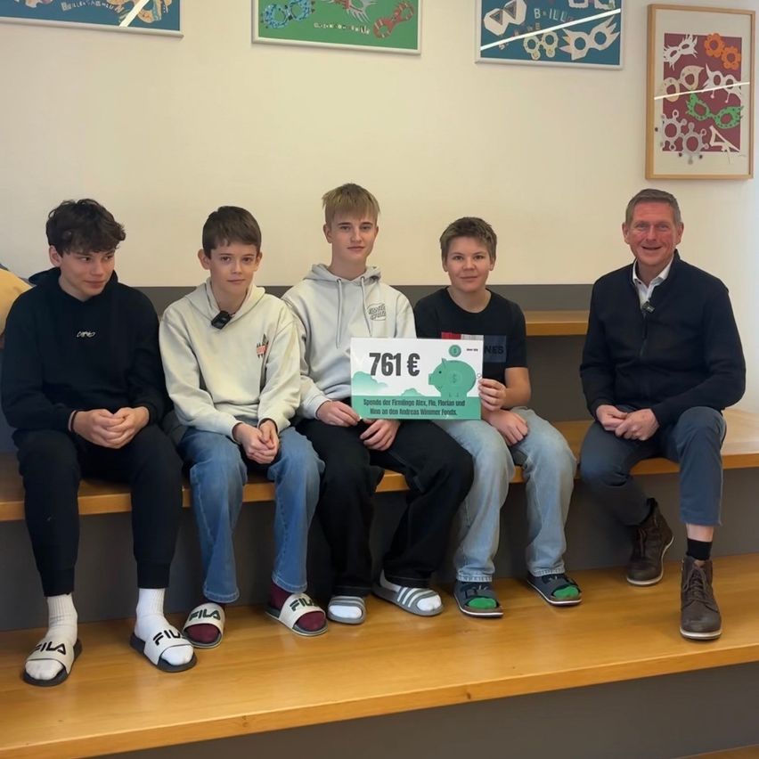 Fünf Jungen sitzen auf einer Bank mit einem Mann, der ein Schild mit 761 Euro hält. Sie alle scheinen für ein Foto zu lächeln.