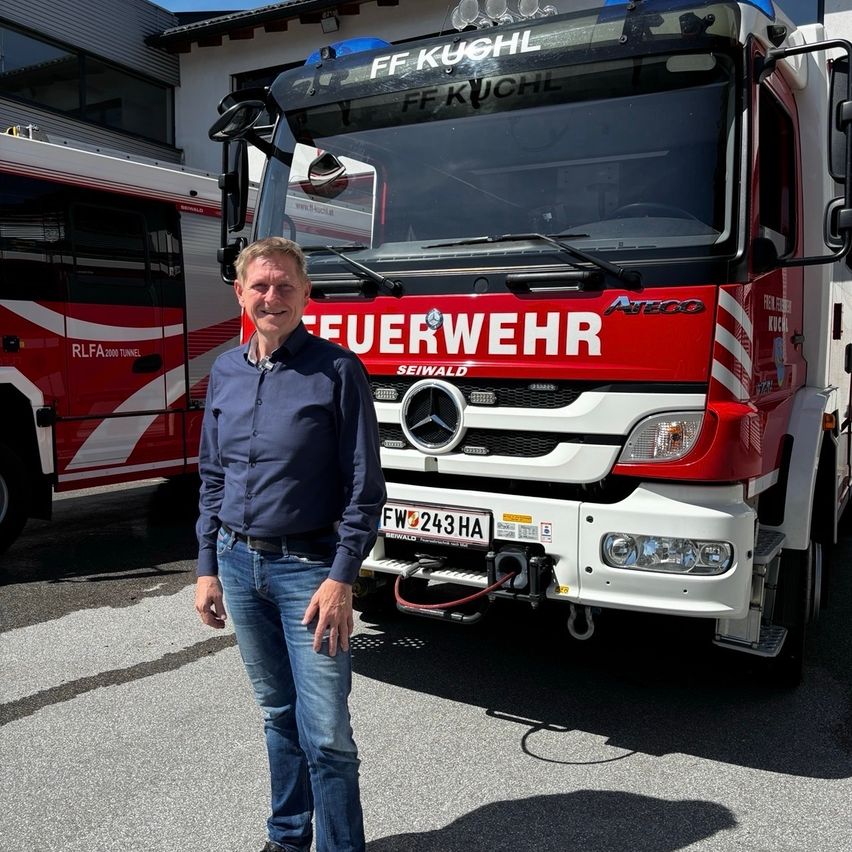 Ein Mann steht lächelnd vor einem roten Feuerwehrauto. Das Fahrzeug hat ein Mercedes-Logo und FF Kuchl auf der Front geschrieben.