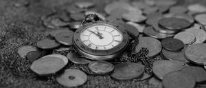 Eine Taschenuhr mit römischen Zahlen liegt auf einem Haufen Münzen und symbolisiert den Wert von Zeit und Geld.