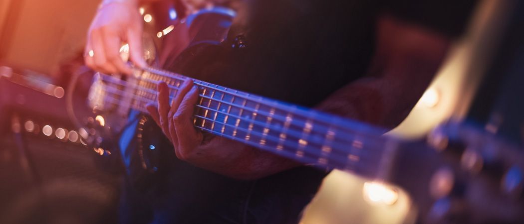 Ein Musiker spielt eine Bassgitarre auf einer Bühne, die von blauen Lichtern beleuchtet wird.