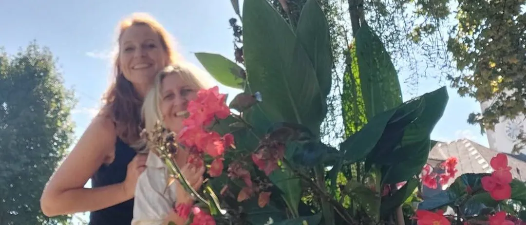 Zwei Frauen stehen hinter einer großen Blumenarrangement, lächeln und posieren für ein Foto.
