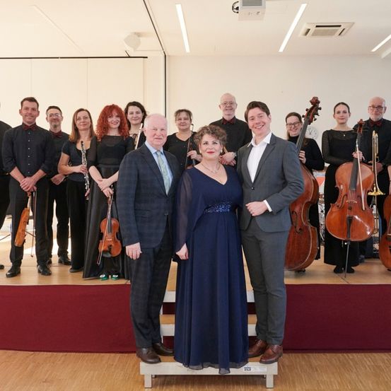 Eine Gruppe von Musikern in formeller Kleidung, steht mit Instrumenten auf der Bühne und posiert für ein Foto.