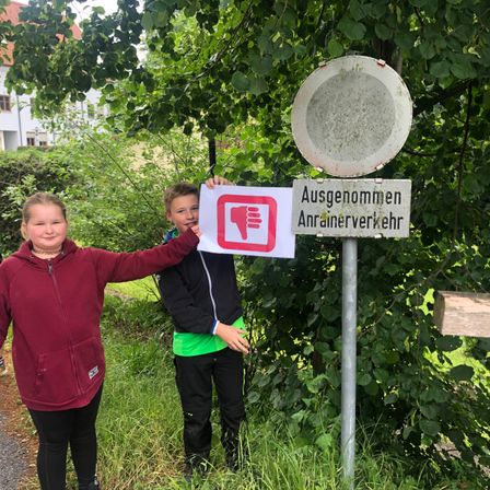 Zwei Kinder stehen neben einem Schild mit einem Verbotssymbol und dem Text 'Ausgenommen Anrainerverkehr'.