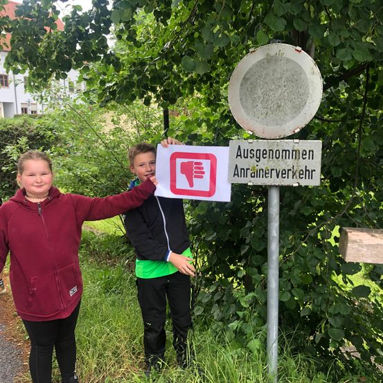 Zwei Kinder stehen neben einem Schild mit einem Verbotssymbol und dem Text 'Ausgenommen Anrainerverkehr'.