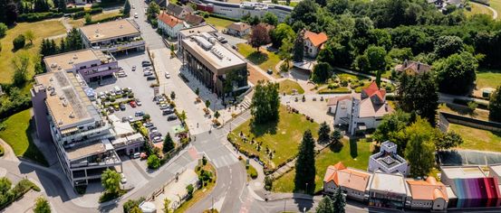 Aerial view of a small town with many buildings and cars parked in the area. Trees and greenery are abundant, and the sky is clear.