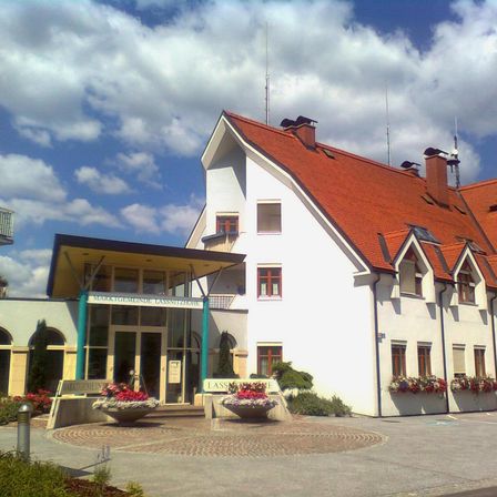 Ein weißes Gebäude mit einem roten Dach und mehreren Fenstern. Es hat zwei Schornsteine oben und mehrere Pflanzen mit Blumen davor.