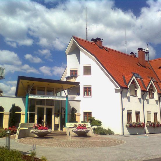 Ein weißes Gebäude mit einem roten Dach und mehreren Fenstern. Es hat zwei Schornsteine oben und mehrere Pflanzen mit Blumen davor.