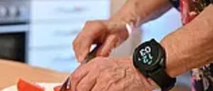 Eine Person schneidet Tomaten auf einem Schneidebrett in einer Küche. Sie trägt eine Uhr am Handgelenk.