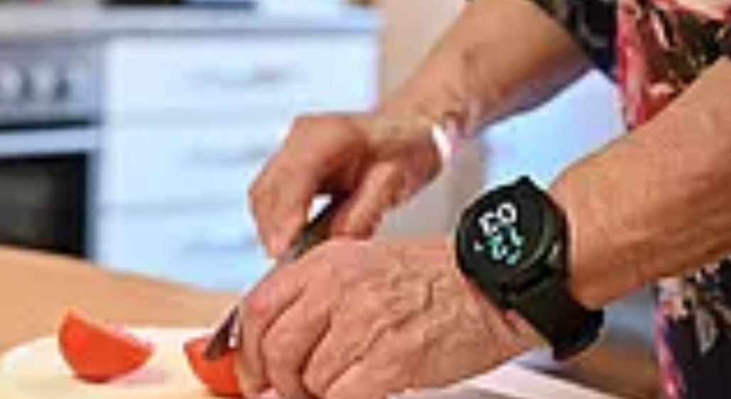 Eine Person schneidet Tomaten auf einem Schneidebrett in einer Küche. Sie trägt eine Uhr am Handgelenk.