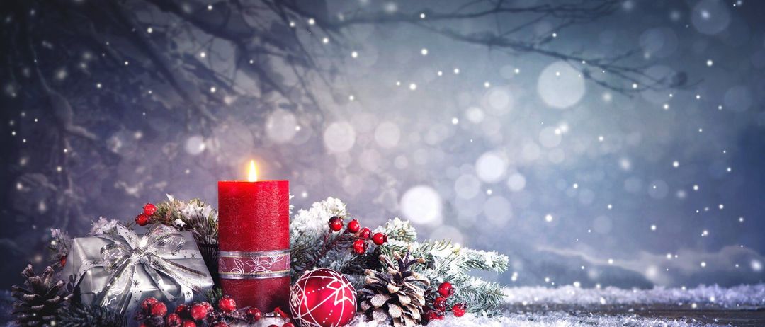 Eine rote Kerze, umgeben von Weihnachtsdekorationen wie Tannenzapfen, Stechbeeren und einer roten Kugel, mit einem verschwommenen verschneiten Hintergrund.