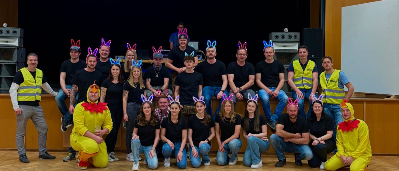 Eine Gruppe von Menschen in Hasenkostümen und schwarzen T-Shirts posiert für ein Foto in einem Studio. Ein Mann in einem gelben Kostüm hockt vorne.
