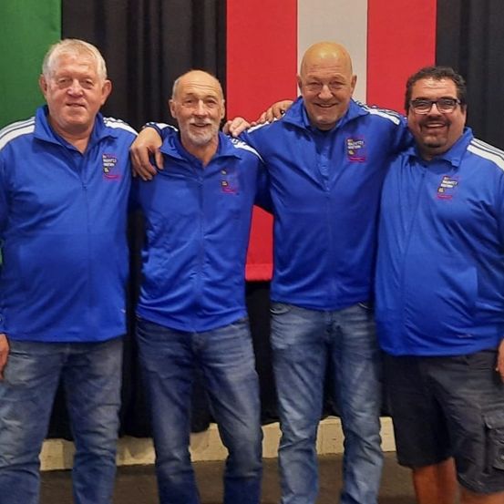 Vier Männer in blauen Jacken mit weißen Streifen stehen zusammen vor einer Kulisse mit der italienischen Flagge.