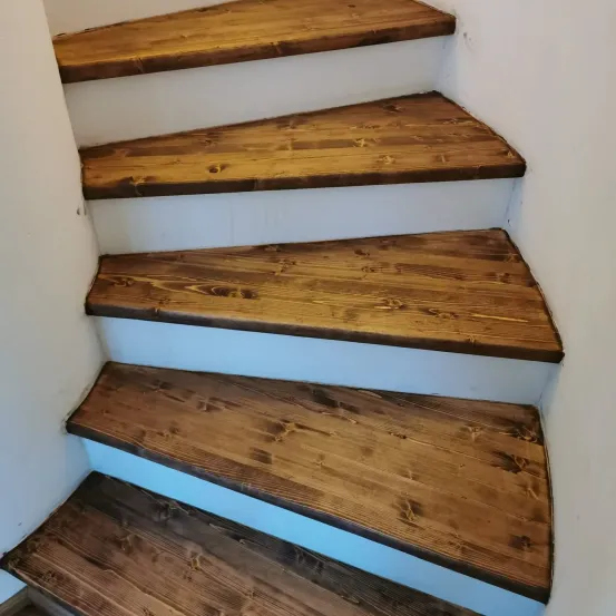 Ein Nahaufnahme einer Holztreppe mit Spiraldesign. Die Stufen bestehen aus Holzbrettern und die Kanten sind weiß gestrichen. Die Holzstruktur ist sichtbar und das Maserungsmuster ist deutlich.
