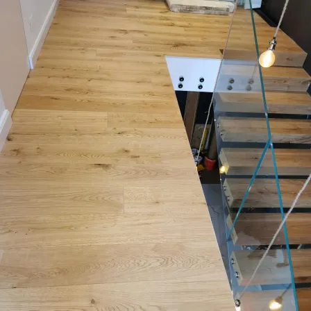 Ein Nahaufnahme eines Holzbodens mit einer Glastreppe auf der rechten Seite. Der Boden hat ein natürliches Holzmaserungsmuster.