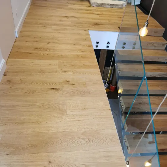 Ein Nahaufnahme eines Holzbodens mit einer Glastreppe auf der rechten Seite. Der Boden hat ein natürliches Holzmaserungsmuster.