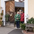 Ein Mann und eine Frau stehen vor einer Holztür mit dem Schild 'Kasa'. Sie lächeln beide und scheinen für ein Foto zu posieren.