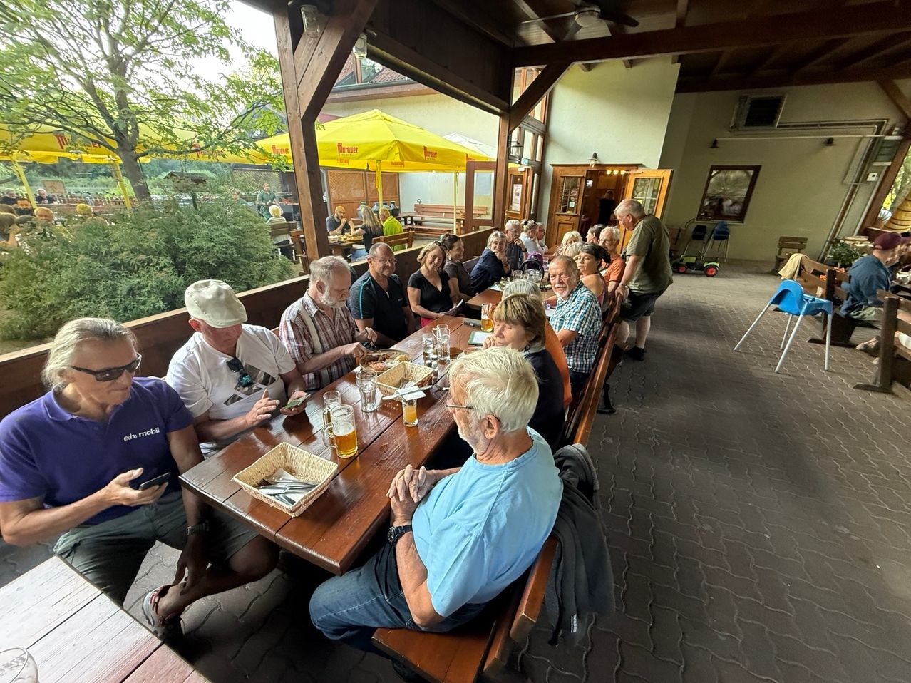 Eine Gruppe von Menschen sitzt an einem Tisch in einem Restaurant im Freien, einige mit Biergläsern und andere mit Handys.