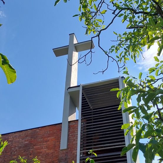 Ein weißes Kreuz auf einem Ziegelgebäude mit einer Metallstruktur und Blättern.