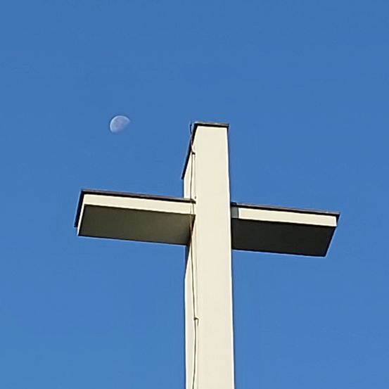 Ein weißes Kreuz mit einem Halbmond im Himmel, vor einem klaren blauen Himmel.
