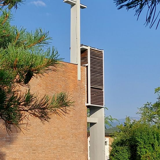 Ein Ziegelgebäude mit einem Turmaufbau ist von Bäumen umgeben und in der Ferne sind Berge zu sehen.