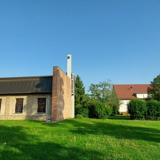 Ein Gebäude mit Ziegelwänden und einem grauen Dach steht auf einem grünen Rasen. Der Himmel ist klar und blau.