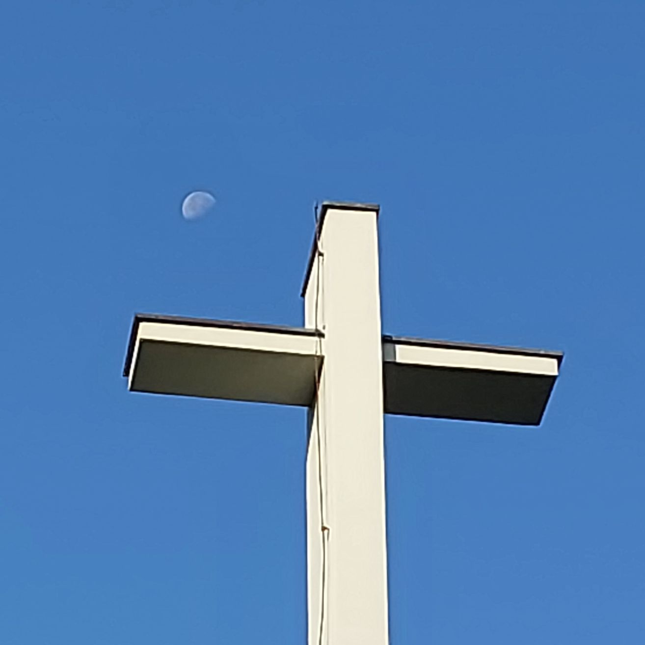 Ein weißes Kreuz vor einem blauen Himmel mit einem Halbmond in der oberen linken Ecke.