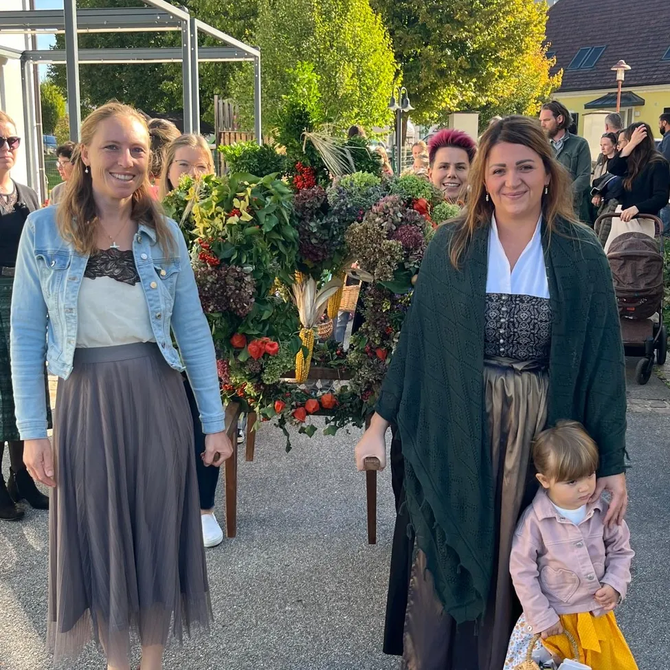 Zwei Frauen und ein Kind stehen vor einem dekorativen Kranz und lächeln für ein Foto.
