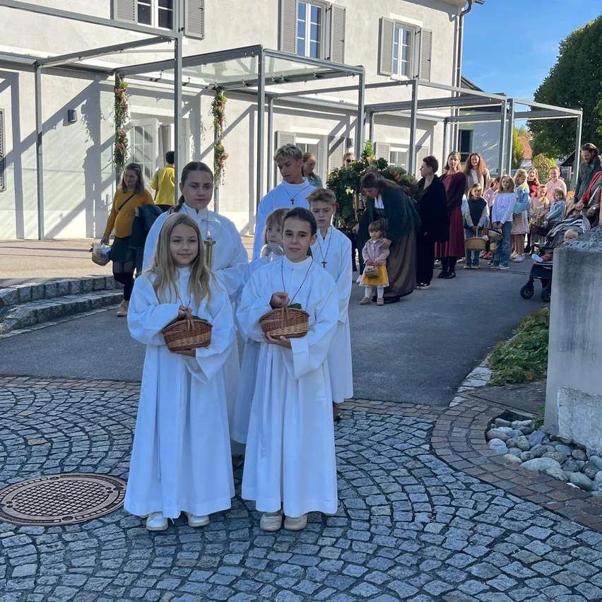 Fünf Kinder in weißen Gewändern und mit Körben stehen vor einem Gebäude.