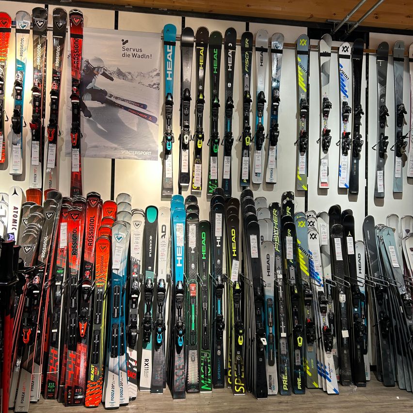 Eine Ausstellung verschiedener Skier und Snowboards, die an einer Wand aufgehängt sind, mit einem Plakat, das Skifahren bewirbt.