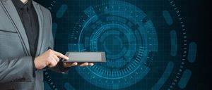 Ein Geschäftsmann in einem Anzug hält ein Tablet mit einer komplexen digitalen Benutzeroberfläche im Hintergrund. Die Benutzeroberfläche ist blau und weiß mit einem kreisförmigen Muster.