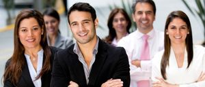 Eine Gruppe von Geschäftsleuten lächelt und posiert für ein Foto mit verschränkten Armen. Ein Mann in einem Anzug steht in der Mitte, und andere stehen hinter ihm.