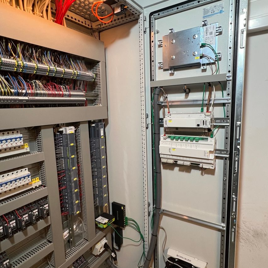 Das Bild zeigt einen Elektroschalter mit zahlreichen Drähten und Komponenten, die an verschiedene Anschlüsse angeschlossen sind. Der Schalter ist an einer Wand montiert und enthält mehrere Leistungsschalter und Sicherungen.