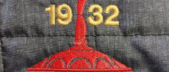 Nahaufnahme eines grauen gesteppten Jackens mit dem gestickten Logo von ESV 1932 Feldkirchen. Das Logo ist rot und hat goldfarbenen Text mit den Zahlen 1932.