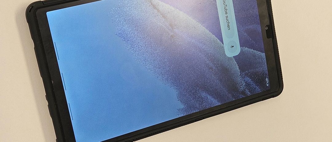 Ein Tablet mit schwarzem Gehäuse wird auf einem hellbeigen Hintergrund angezeigt. Der Bildschirm zeigt ein YouTube-Video, das abgespielt wird.