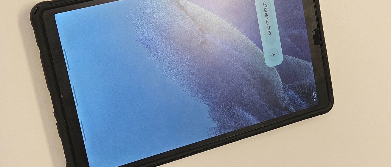 Ein Tablet mit schwarzem Gehäuse wird auf einem hellbeigen Hintergrund angezeigt. Der Bildschirm zeigt ein YouTube-Video, das abgespielt wird.