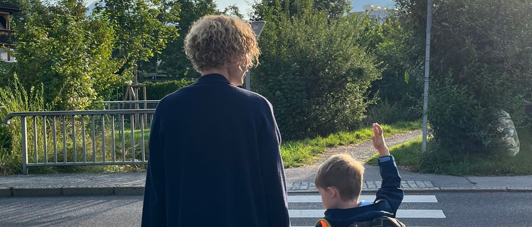 Eine Frau und ein Junge überqueren die Straße an einem Zebrastreifen. Der Junge hat einen Rucksack.