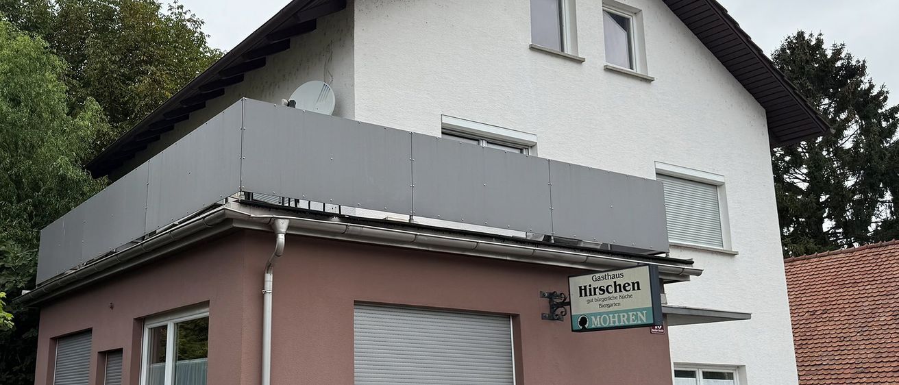 Das Bild zeigt ein zweistöckiges Gebäude mit einem grauen Dach und rosa Wänden. Das Gebäude hat mehrere Fenster und ein kleines Schild mit den Worten Hirschen und Mohren.