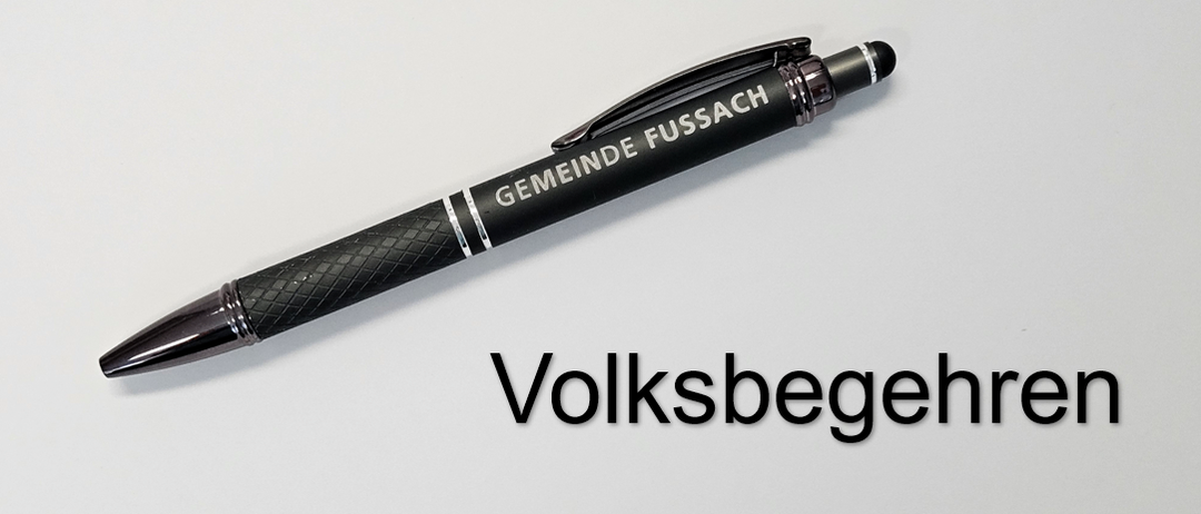 Ein schwarzer Stift mit silbernem Akzent ist mit 'Gemeinde Fussach' beschriftet. Er liegt auf einem weißen Hintergrund, unter dem der Text 'Volksbegeher' steht.
