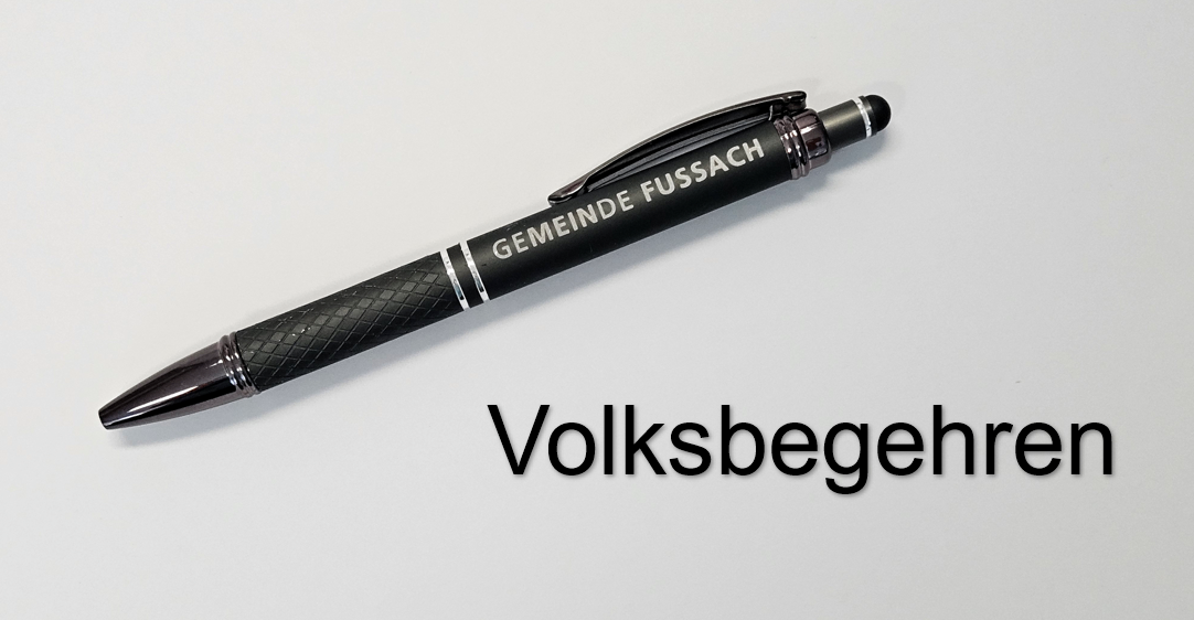 Ein schwarzer Stift mit silbernem Akzent ist mit 'Gemeinde Fussach' beschriftet. Er liegt auf einem weißen Hintergrund, unter dem der Text 'Volksbegeher' steht.