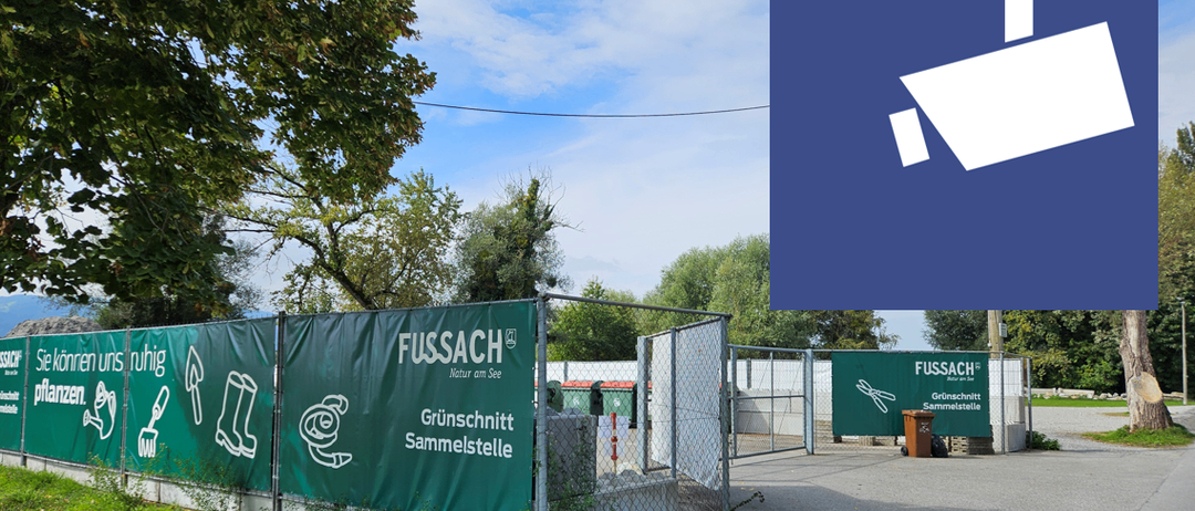 Eine grüne Umzäunung mit 'FUSSAC' Logo und der Aufschrift 'Grünschnitt Sammelstelle'. Ein Mülleimer steht neben dem Tor. Ein klarer Himmel mit Wolken.