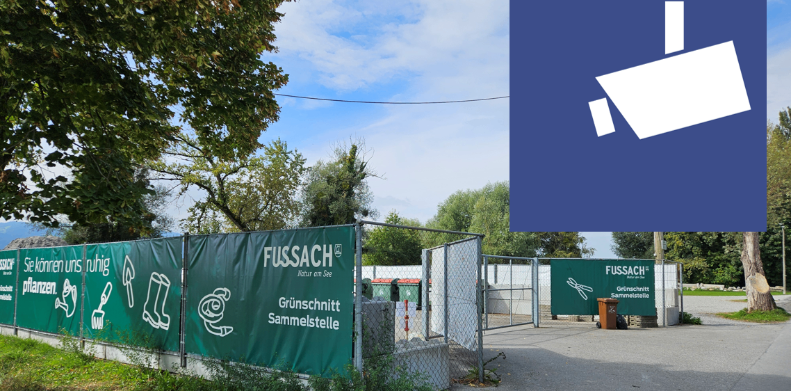 Eine grüne Umzäunung mit 'FUSSAC' Logo und der Aufschrift 'Grünschnitt Sammelstelle'. Ein Mülleimer steht neben dem Tor. Ein klarer Himmel mit Wolken.