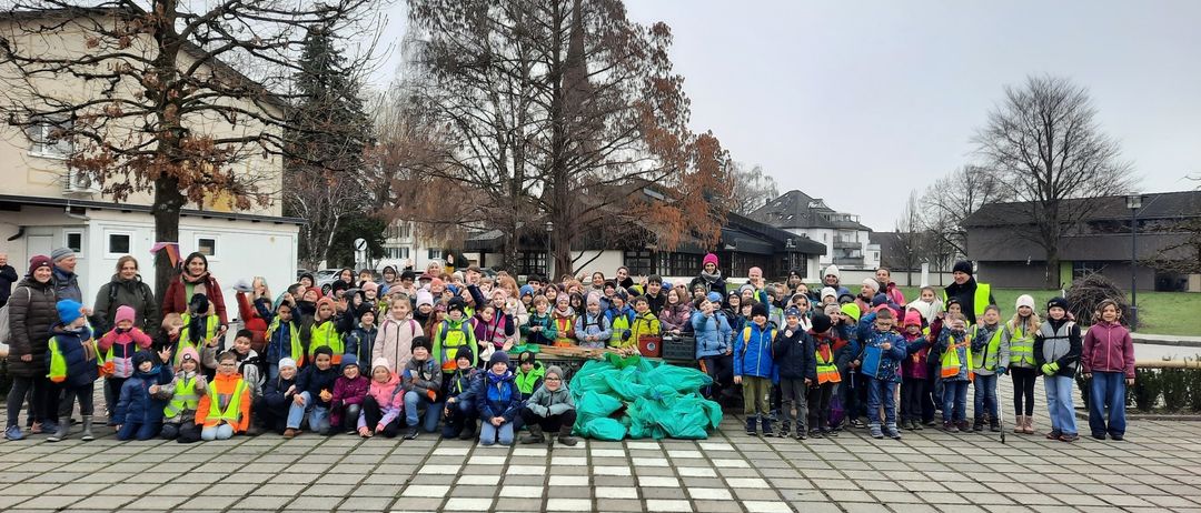Eine Gruppe von Kindern und Erwachsenen in Sicherheitswesten posiert für ein Foto im Freien mit mehreren Bäumen im Hintergrund.