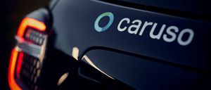 Ein Nahaufnahme des Hecks eines schwarzen Autos mit dem Logo 'O carus' in Weiß auf dunklem Hintergrund. Die Rückleuchte des Autos befindet sich auf der linken Seite.