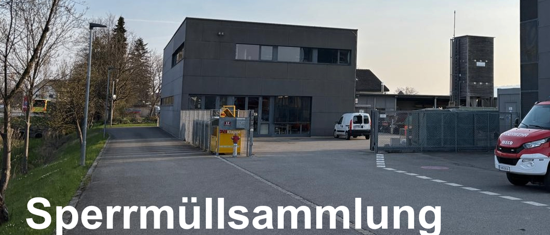 Ein großes graues Gebäude mit mehreren Fenstern und einem weißen Lieferwagen davor. Das Gebäude hat einen gelben Container mit einer roten Figur darauf. Das Gebiet ist von einem Zaun und Bäumen umgeben. Das Wort 'rmüllsammelung' ist auf dem Boden geschrieben.