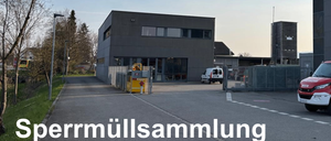 Ein großes graues Gebäude mit mehreren Fenstern und einem weißen Lieferwagen davor. Das Gebäude hat einen gelben Container mit einer roten Figur darauf. Das Gebiet ist von einem Zaun und Bäumen umgeben. Das Wort 'rmüllsammelung' ist auf dem Boden geschrieben.