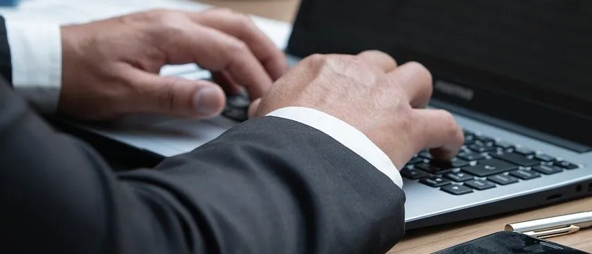 Eine Person in Anzug tippt auf einen Laptop, mit einer Statue der Gerechtigkeit hinter ihr auf einem Schreibtisch.