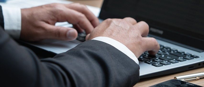 Eine Person in Anzug tippt auf einen Laptop, mit einer Statue der Gerechtigkeit hinter ihr auf einem Schreibtisch.