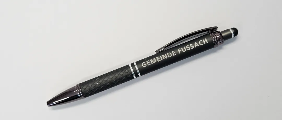 Ein schwarzer Stift mit silbernen Akzenten und der Aufschrift 'GEMEINDE FUSSAC'. Der Stift hat einen schwarzen Griff und eine silberne Spitze.